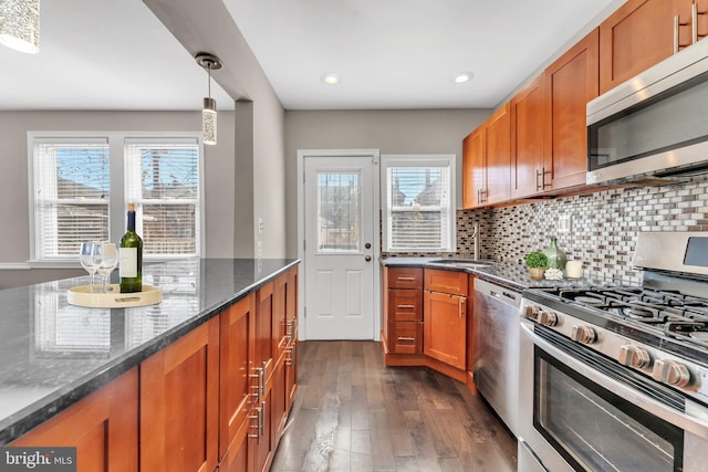 kitchen featuring stainless steel appliances, dark stone countertops, sink, pendant lighting, and dark hardwood / wood-style flooring