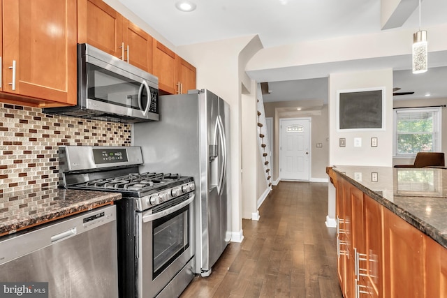 kitchen with tasteful backsplash, hanging light fixtures, stainless steel appliances, dark wood-type flooring, and dark stone countertops