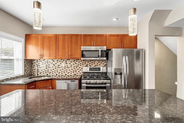 kitchen with hanging light fixtures, backsplash, appliances with stainless steel finishes, dark stone counters, and sink