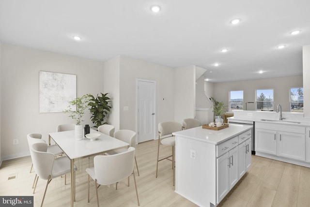 kitchen featuring a center island, light hardwood / wood-style floors, white cabinetry, a breakfast bar area, and sink