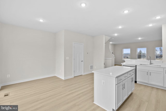 kitchen featuring white cabinets, light hardwood / wood-style floors, a center island, dishwashing machine, and sink