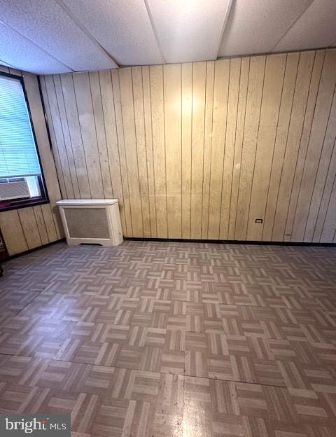 basement featuring wooden walls, a drop ceiling, and parquet floors