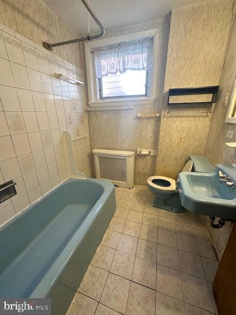 full bathroom with sink, radiator heating unit, toilet, tile walls, and tiled shower / bath