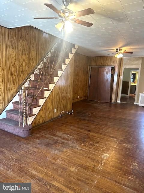 interior space featuring dark wood-type flooring, ceiling fan, and wood walls