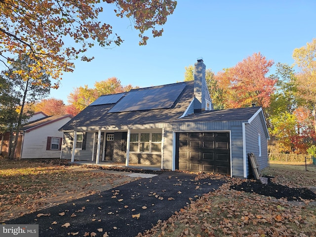 back of house with covered porch, solar panels, and a garage