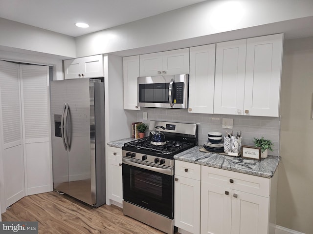 kitchen featuring white cabinetry, light stone counters, stainless steel appliances, and light wood-type flooring