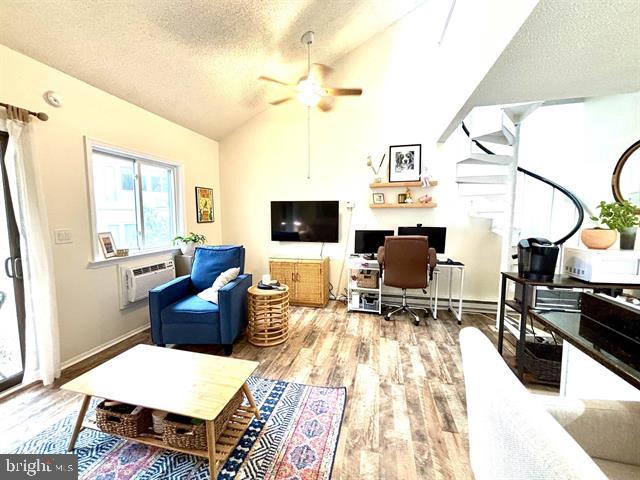 living room with ceiling fan, a textured ceiling, wood-type flooring, vaulted ceiling, and an AC wall unit