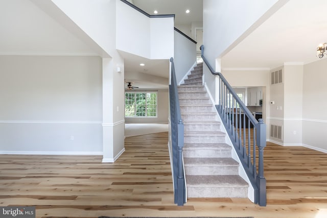 staircase featuring ornamental molding, hardwood / wood-style flooring, high vaulted ceiling, and ceiling fan with notable chandelier