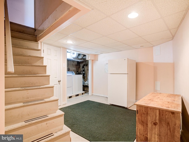 basement with a paneled ceiling, white fridge, and washing machine and clothes dryer