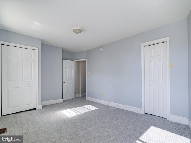 unfurnished bedroom with multiple closets and light colored carpet