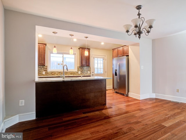 kitchen with hardwood / wood-style flooring, backsplash, stainless steel fridge, a notable chandelier, and decorative light fixtures