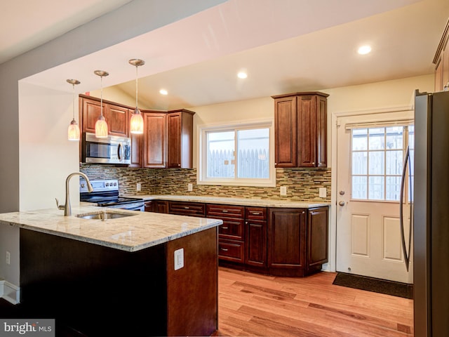 kitchen with pendant lighting, light wood-type flooring, stainless steel appliances, and kitchen peninsula