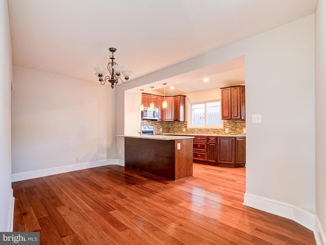 kitchen with kitchen peninsula, light hardwood / wood-style floors, pendant lighting, decorative backsplash, and a chandelier