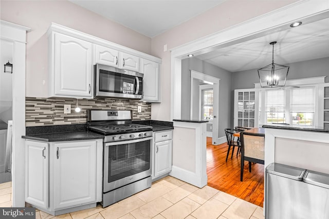 kitchen featuring appliances with stainless steel finishes, light wood-type flooring, decorative light fixtures, white cabinets, and a notable chandelier