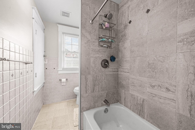 bathroom featuring toilet, tiled shower / bath combo, and tile walls