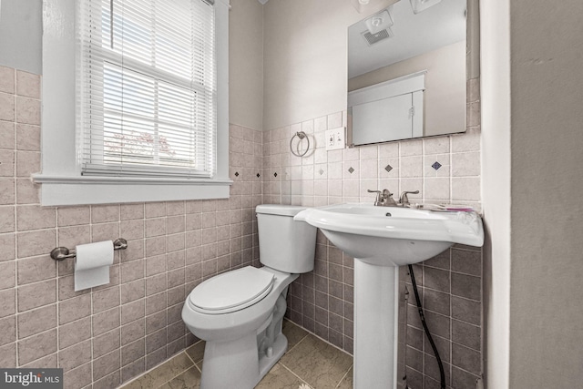 bathroom with tile patterned flooring, toilet, tile walls, and plenty of natural light