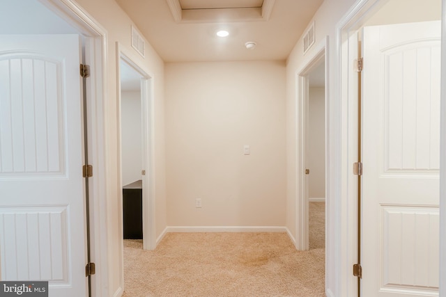 corridor featuring light colored carpet and a tray ceiling