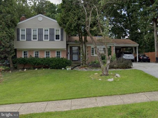 tri-level home featuring brick siding, a chimney, an attached carport, driveway, and a front lawn