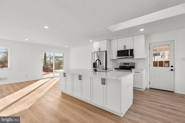 kitchen featuring stainless steel appliances, light countertops, light wood-style floors, white cabinetry, and a sink