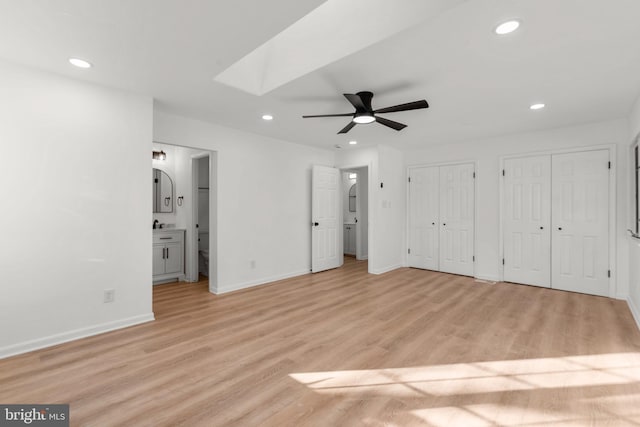 unfurnished bedroom with light wood-style flooring, recessed lighting, a skylight, baseboards, and multiple closets