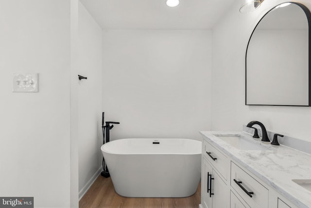 full bath featuring double vanity, baseboards, wood finished floors, a freestanding bath, and a sink