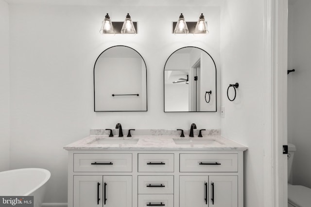 full bath with a freestanding bath, double vanity, a sink, and toilet