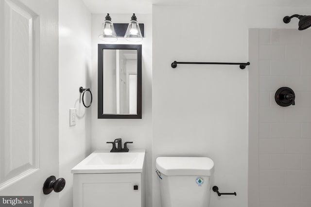 bathroom with toilet, tiled shower, and vanity