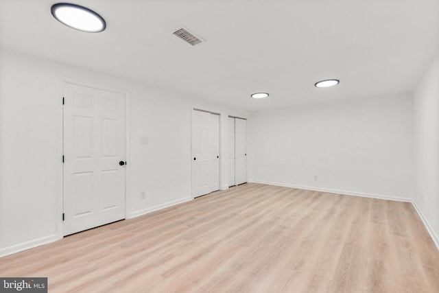 unfurnished bedroom featuring baseboards, light wood-style flooring, visible vents, and multiple closets