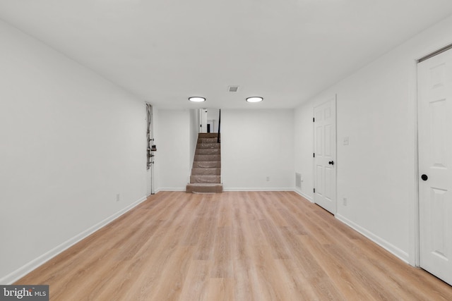 empty room with light wood-style flooring, visible vents, stairway, and baseboards