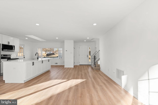 interior space featuring a center island with sink, stainless steel appliances, white cabinetry, a sink, and light wood-type flooring