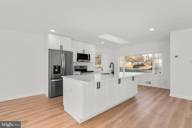 kitchen with stainless steel appliances, a skylight, a sink, visible vents, and a center island with sink