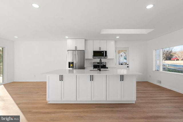 kitchen featuring stainless steel appliances, light countertops, light wood-type flooring, white cabinetry, and a sink