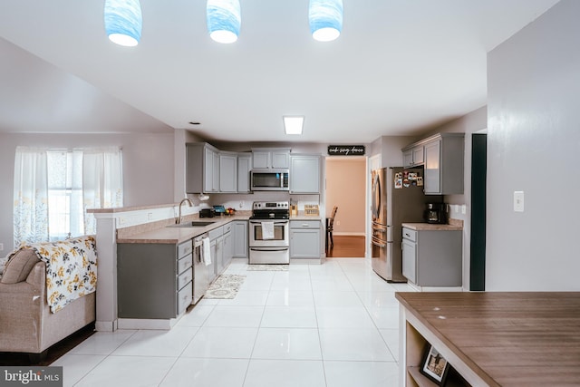 kitchen featuring hanging light fixtures, light tile patterned floors, sink, gray cabinetry, and stainless steel appliances