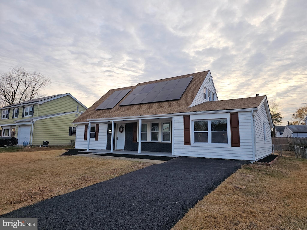 view of front of house with a porch, a yard, and solar panels