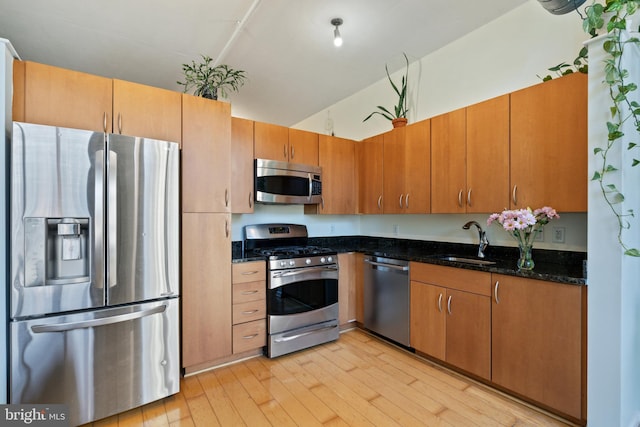 kitchen with dark stone counters, vaulted ceiling, sink, light hardwood / wood-style floors, and stainless steel appliances