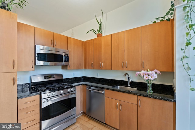 kitchen with appliances with stainless steel finishes, light hardwood / wood-style flooring, dark stone countertops, and sink