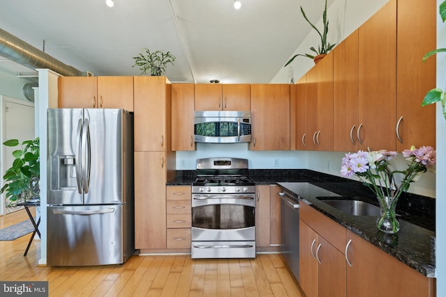 kitchen with appliances with stainless steel finishes, light hardwood / wood-style floors, and dark stone countertops