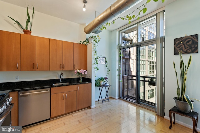 kitchen with sink, appliances with stainless steel finishes, light hardwood / wood-style flooring, and dark stone countertops