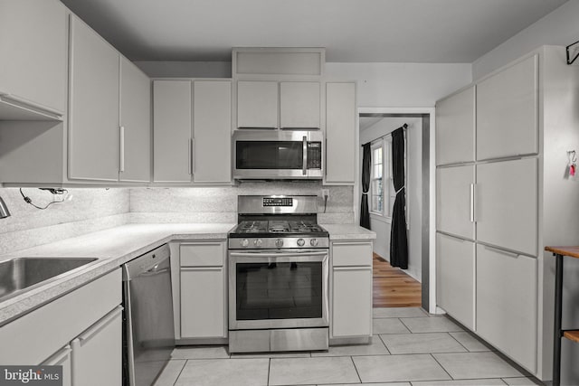 kitchen featuring stainless steel appliances, backsplash, sink, light tile patterned floors, and white cabinets