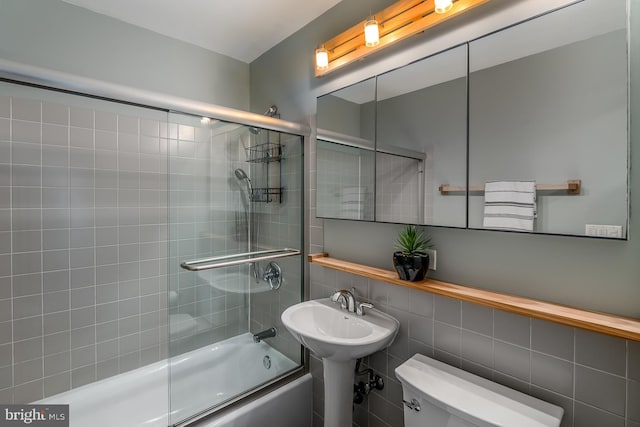 bathroom with tile walls, combined bath / shower with glass door, and toilet