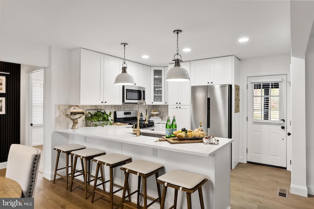 kitchen featuring decorative light fixtures, light wood-type flooring, stainless steel appliances, and white cabinetry