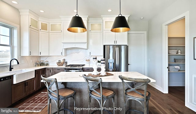 kitchen with light stone countertops, sink, a kitchen island, hanging light fixtures, and stainless steel appliances