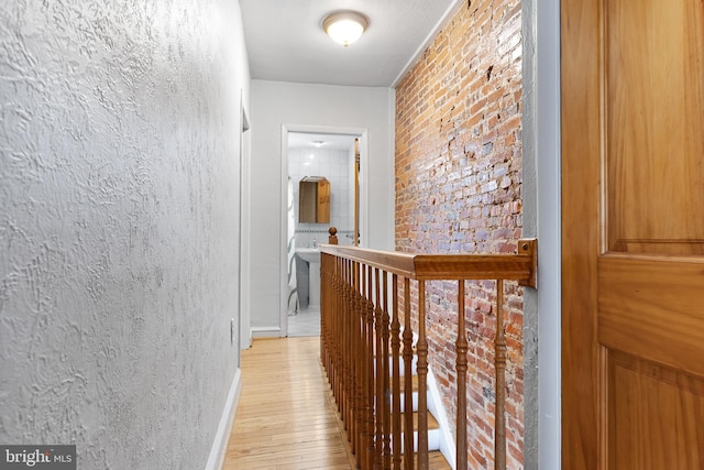 hallway with brick wall and light hardwood / wood-style flooring