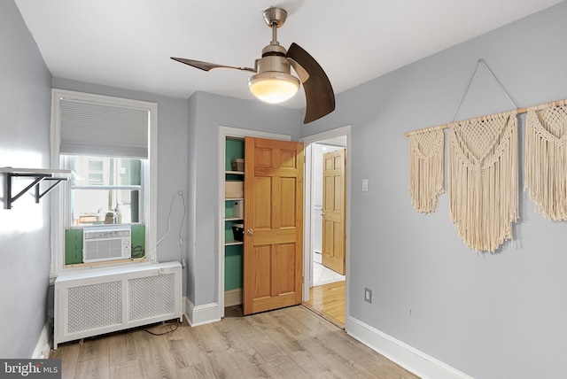 unfurnished bedroom featuring cooling unit, radiator heating unit, light wood-type flooring, and ceiling fan