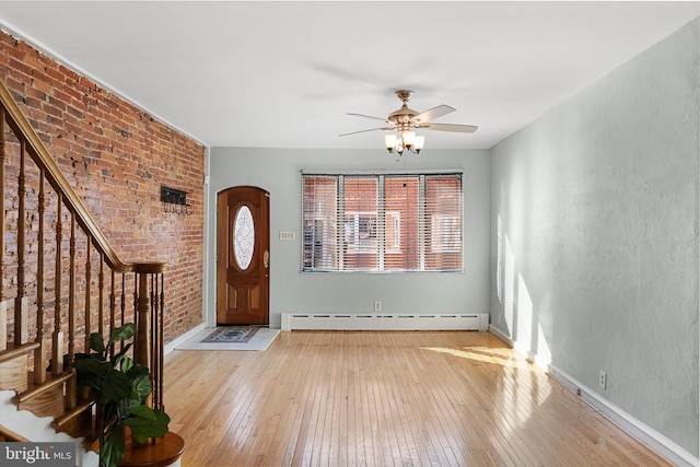 entrance foyer featuring baseboard heating, brick wall, light wood-type flooring, and ceiling fan