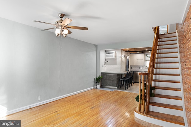 unfurnished living room featuring brick wall, a wall mounted air conditioner, light hardwood / wood-style floors, and ceiling fan