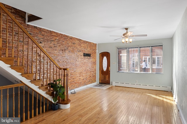 foyer with baseboard heating, brick wall, hardwood / wood-style flooring, and ceiling fan