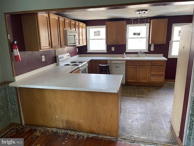 kitchen featuring a sink, brown cabinets, white appliances, baseboards, and light countertops