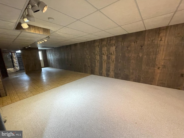 basement with carpet flooring, a paneled ceiling, and wooden walls