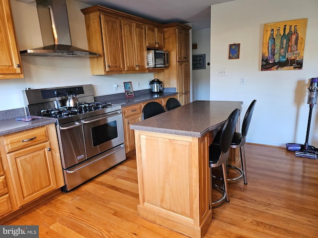 kitchen with wall chimney exhaust hood, a breakfast bar, a center island, appliances with stainless steel finishes, and light hardwood / wood-style floors